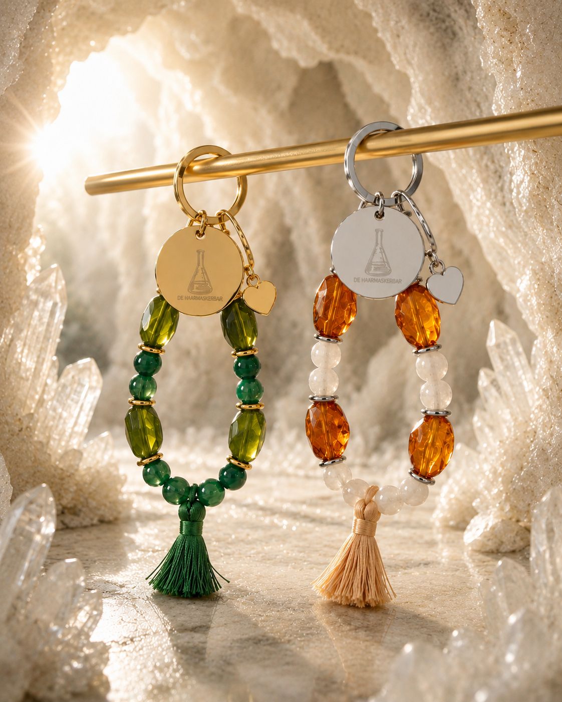 Twee sleutelhangers met De Haarmaskerbar logo in goud en zilver